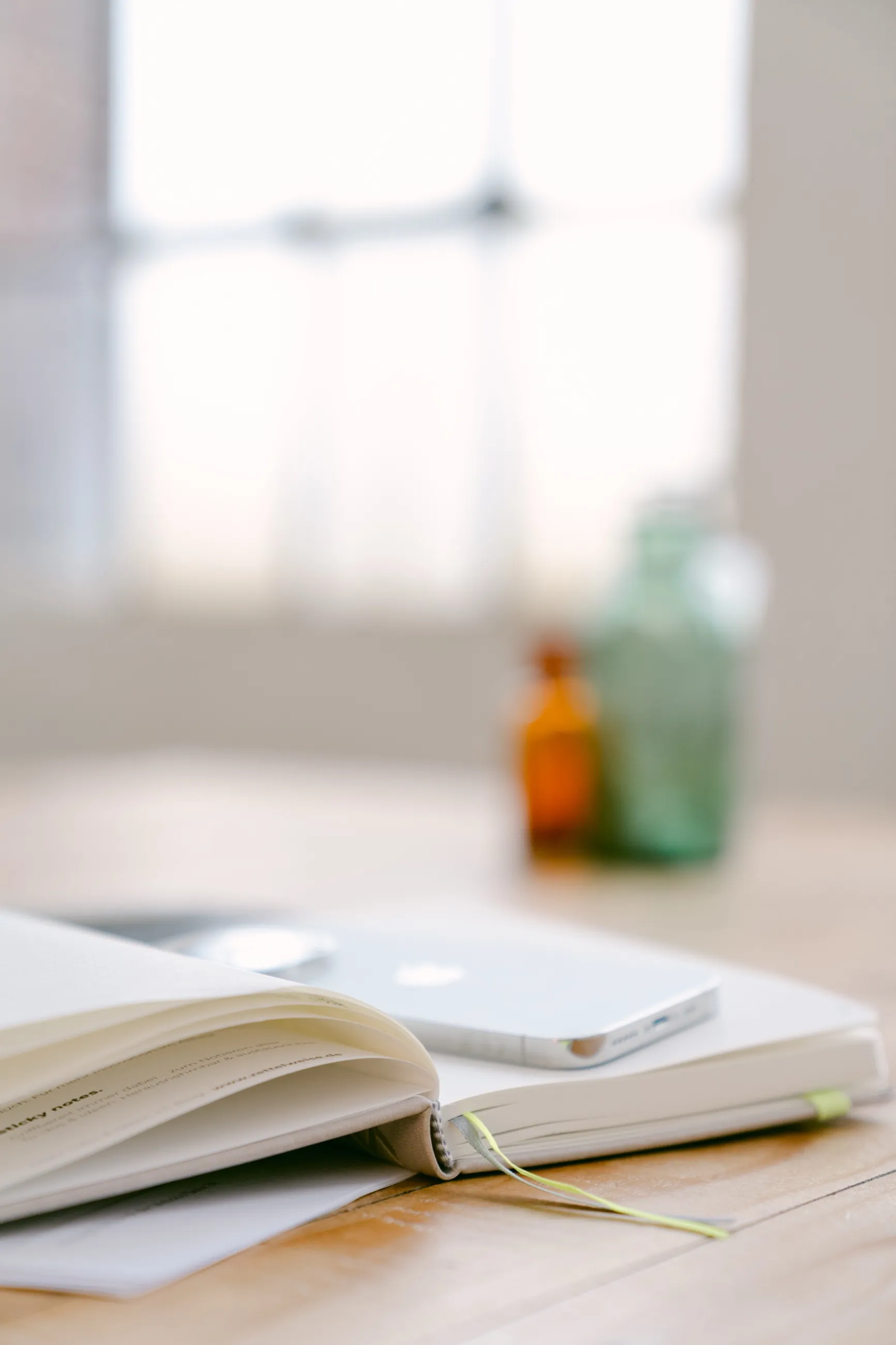 Aufgeschlagenes Notizbuch mit Smartphone auf einem Holztisch, dahinter Apothekerflaschen