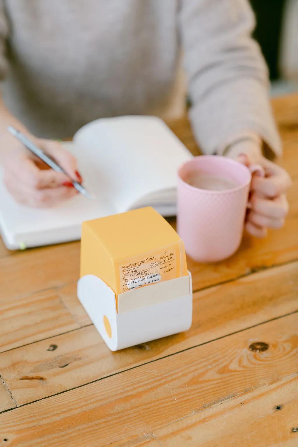 Hände mit Stift über einem Notizbuch, daneben eine Tasse und ein gelber Zettelblock