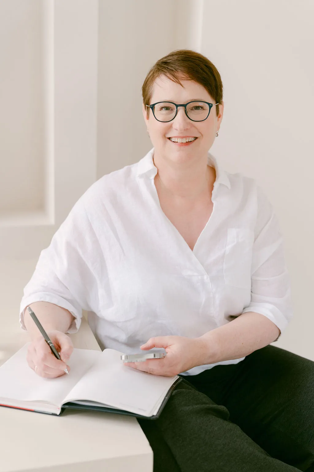 Dr. Ute Heeger in weißer Bluse, lächelnd mit Notizbuch und Stift